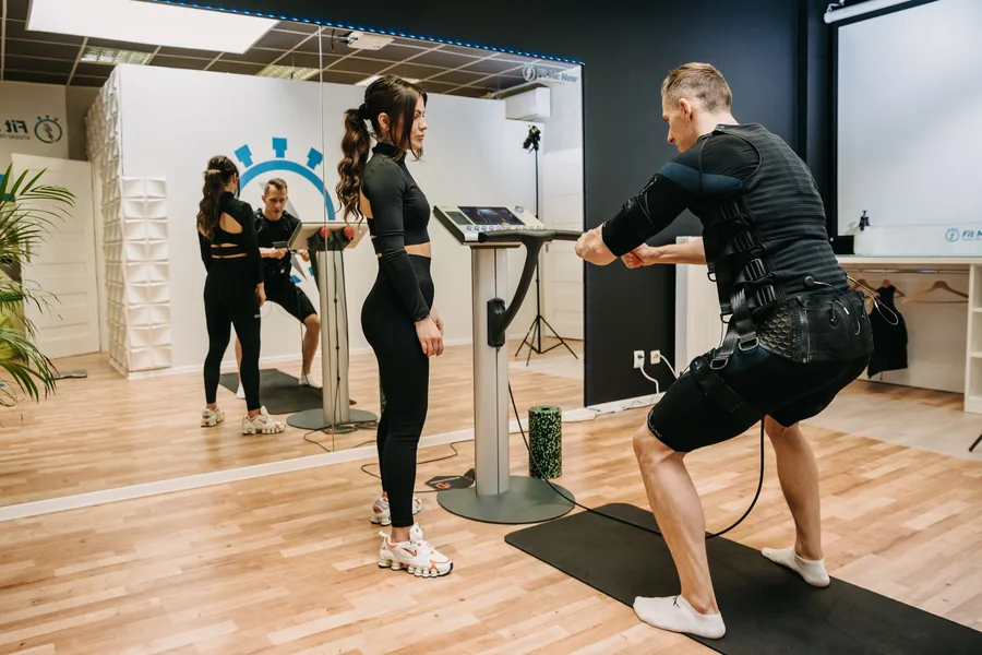 Klienci w kombinezonach EMS wykonują ćwiczenia pod okiem trenera w studiu Fit Me Now