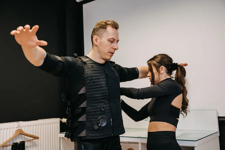 Trener zakłada klientce kombinezon EMS przed treningiem